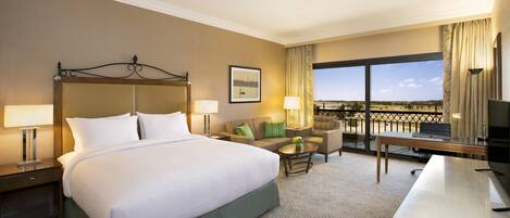 A hotel room with a large bed, a desk, a chair, a sofa, and a balcony with a view.