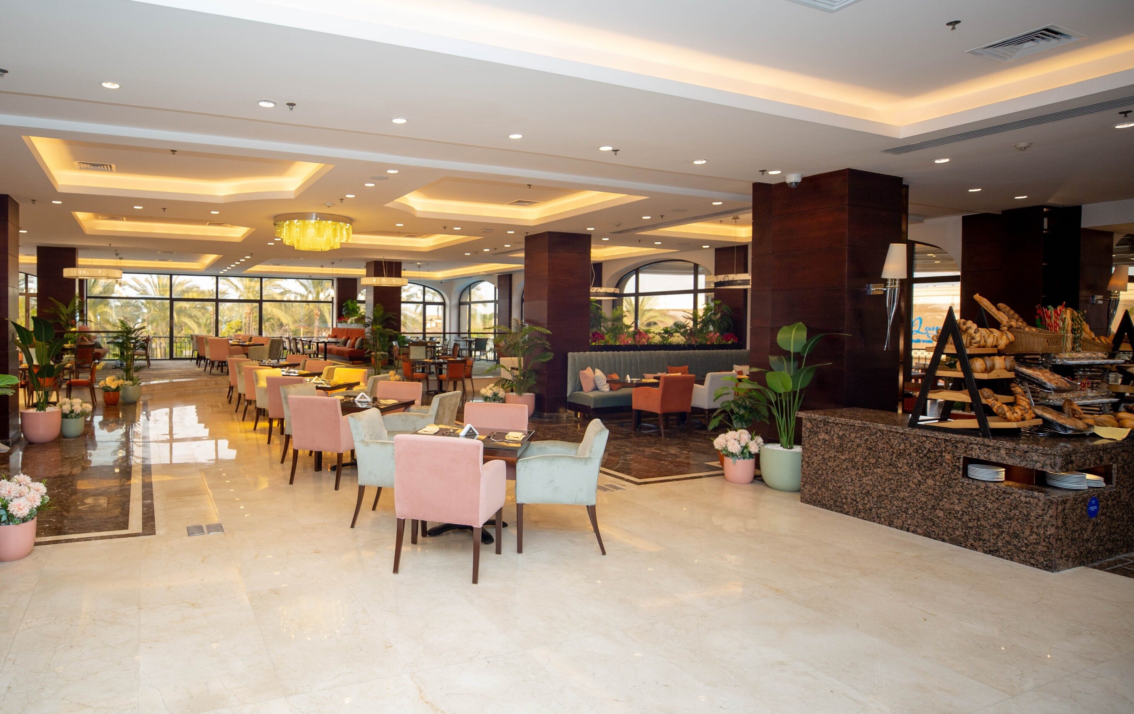 A spacious hotel lobby with multiple seating areas, a central reception desk, and large windows offering views of palm trees.