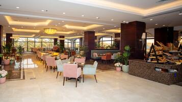 A spacious hotel lobby with multiple seating areas, a central reception desk, and large windows offering views of palm trees.