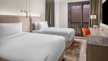 A hotel room with two beds, a desk, a chair, a TV, and a balcony with curtains.