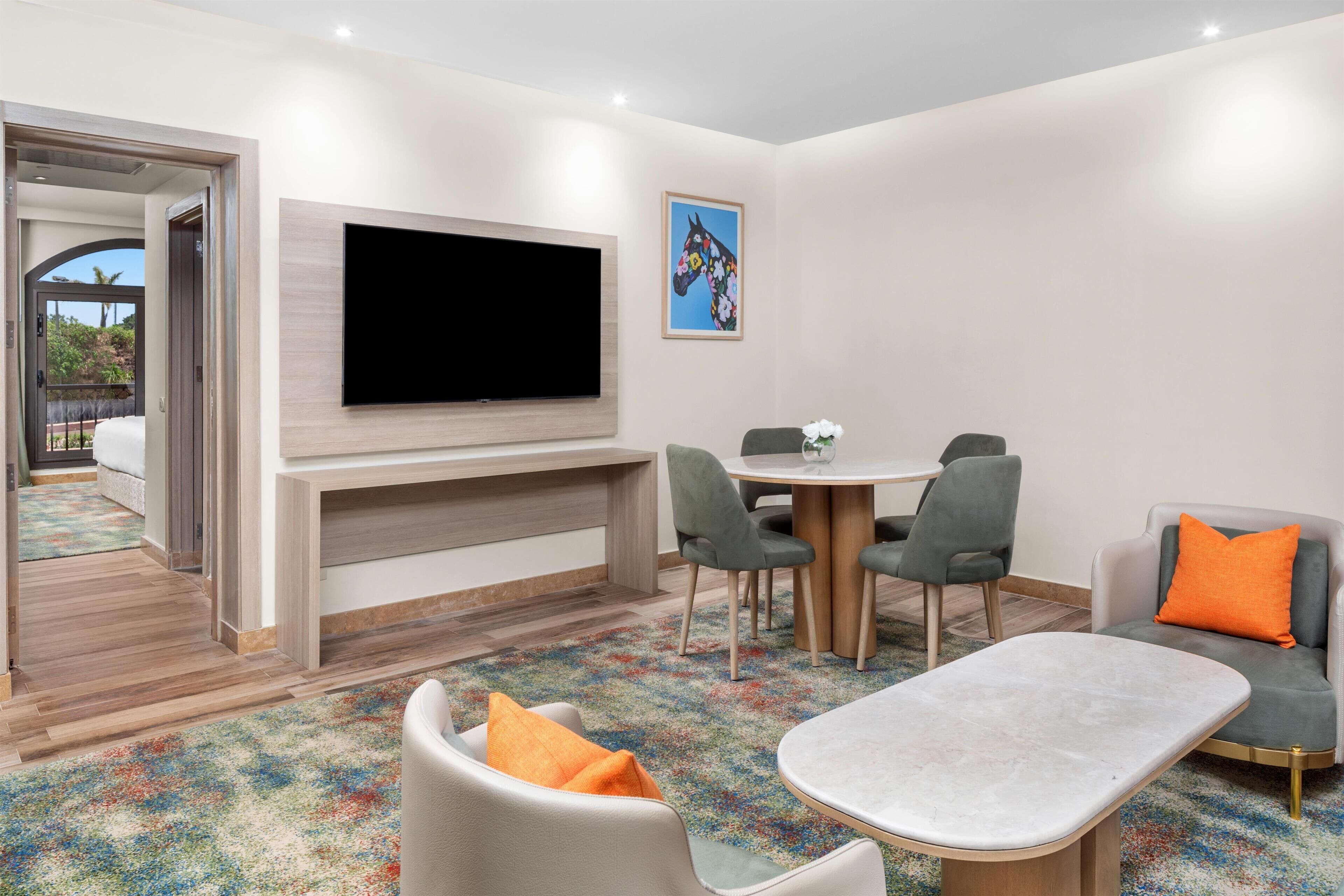 Una sala moderna con televisor de pantalla plana, un comedor con sillas y un sofá con cojín.
