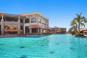 Ett semesterhotell med en stor pool, flera byggnader med balkonger och palmer.