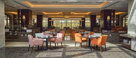 A spacious dining area with multiple tables and chairs, a central chandelier, and large windows providing natural light.