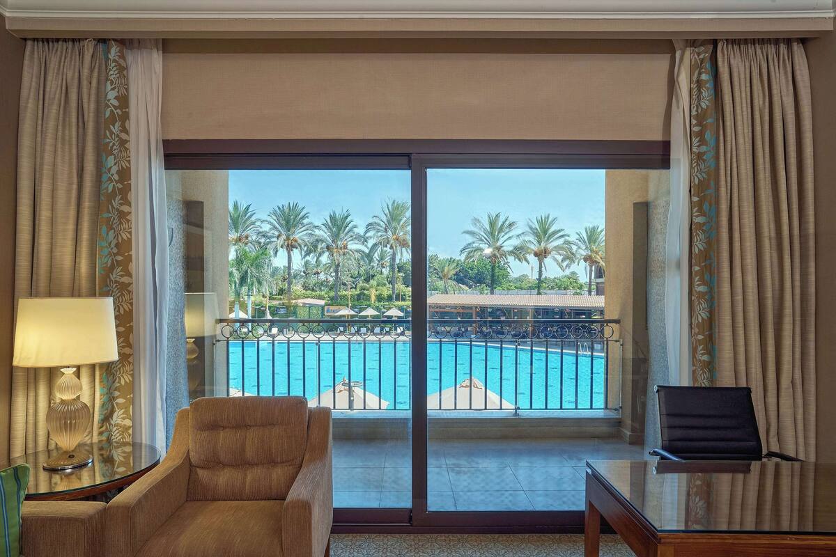 Une chambre d’hôtel avec vue sur une piscine, comprenant une chaise, une table et une lampe.