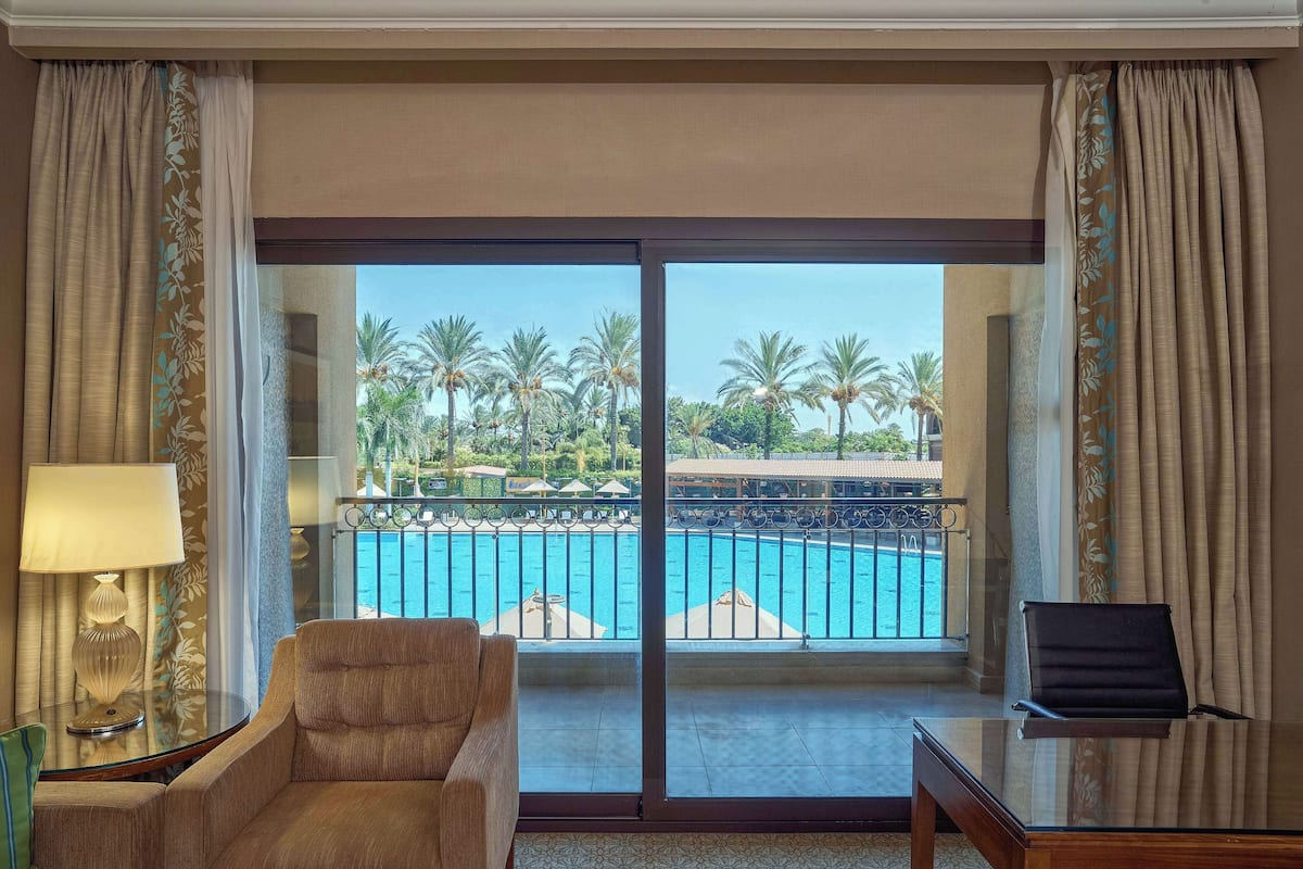 Ein Hotelzimmer mit Blick auf einen Swimmingpool, einem Sessel, einem Tisch und einer Lampe.