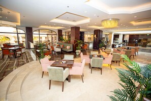 En rymlig hotellobby med flera sittgrupper, en receptionsdisk och stora fönster som erbjuder utsikt över omgivningarna.