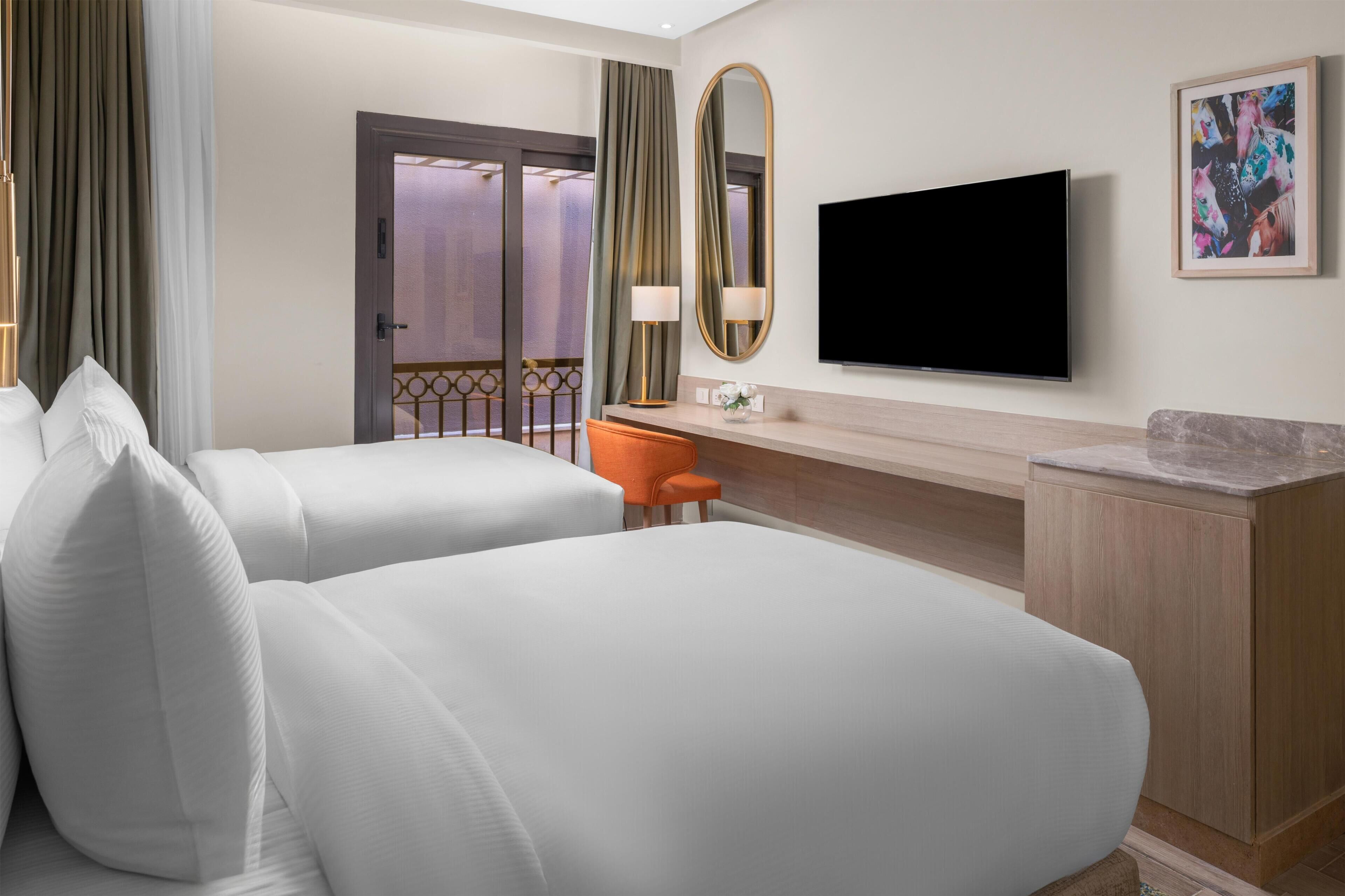 A hotel room with two beds, a desk, a television, and a framed picture on the wall.