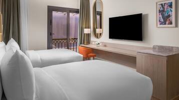 A hotel room with two beds, a desk, a television, and a framed picture on the wall.