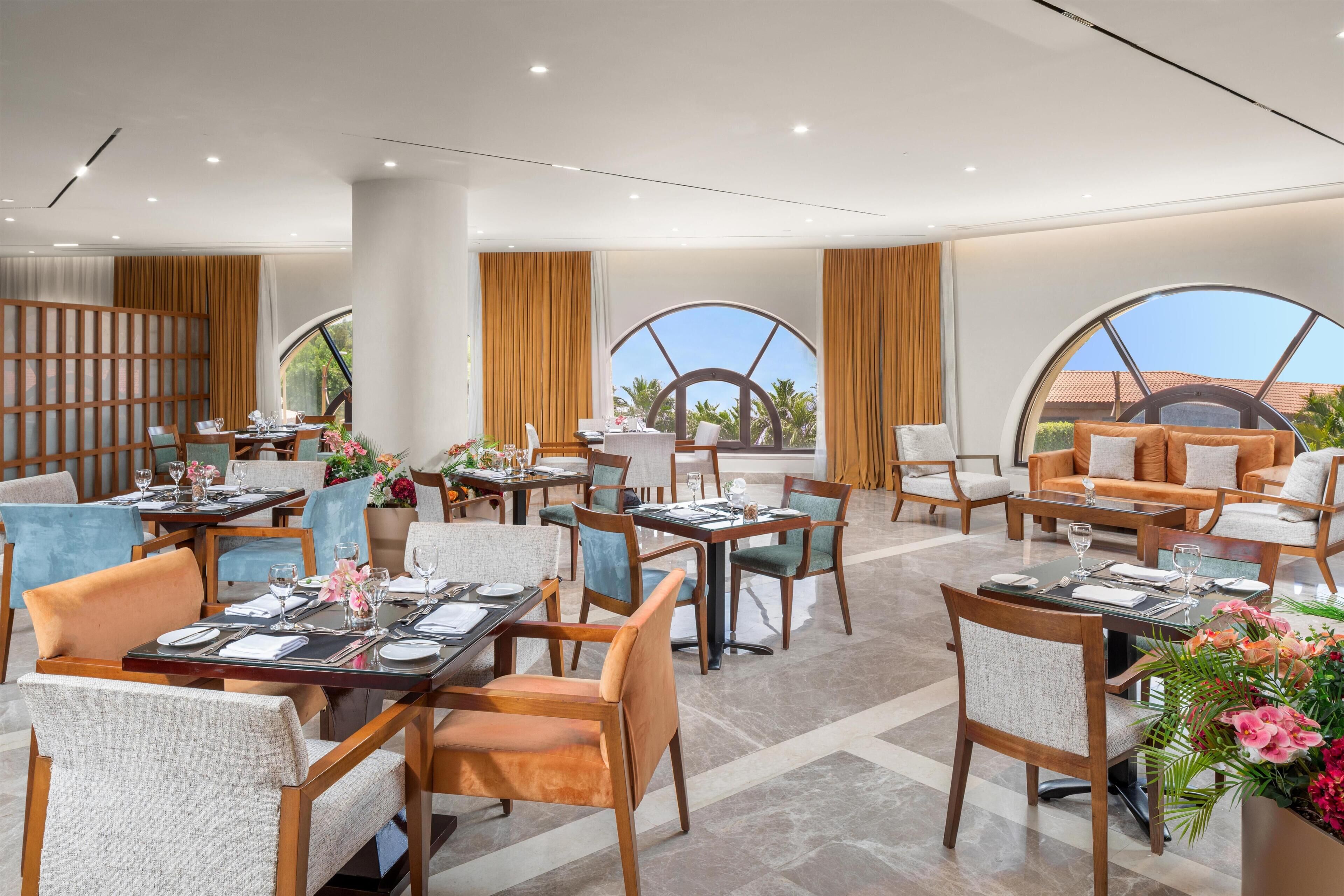 En hotellrestaurang med flera bord och stolar, stora fönster och utsikt över omgivningarna.
