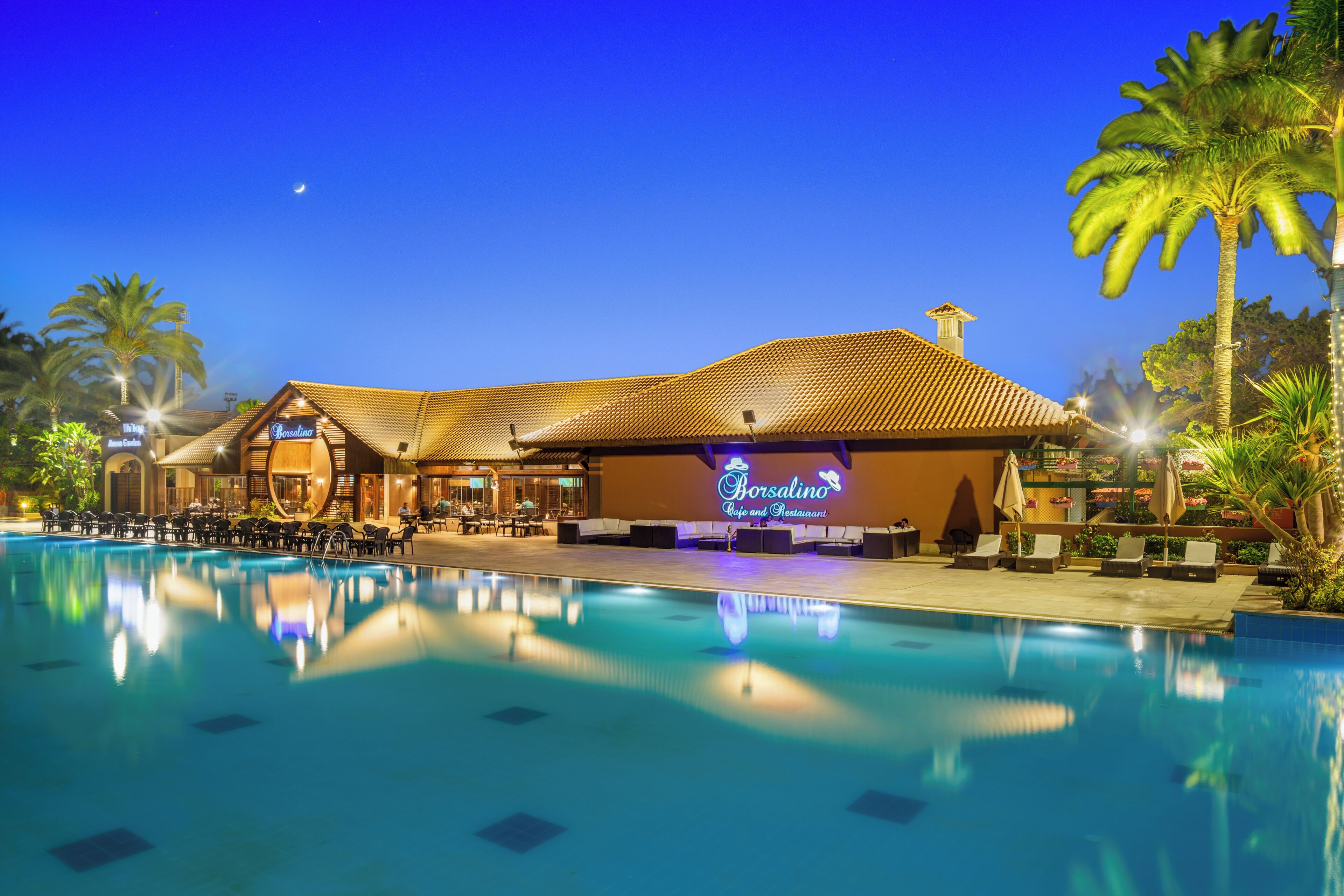 Un hotel con piscina, mobiliario exterior y un letrero de neón.