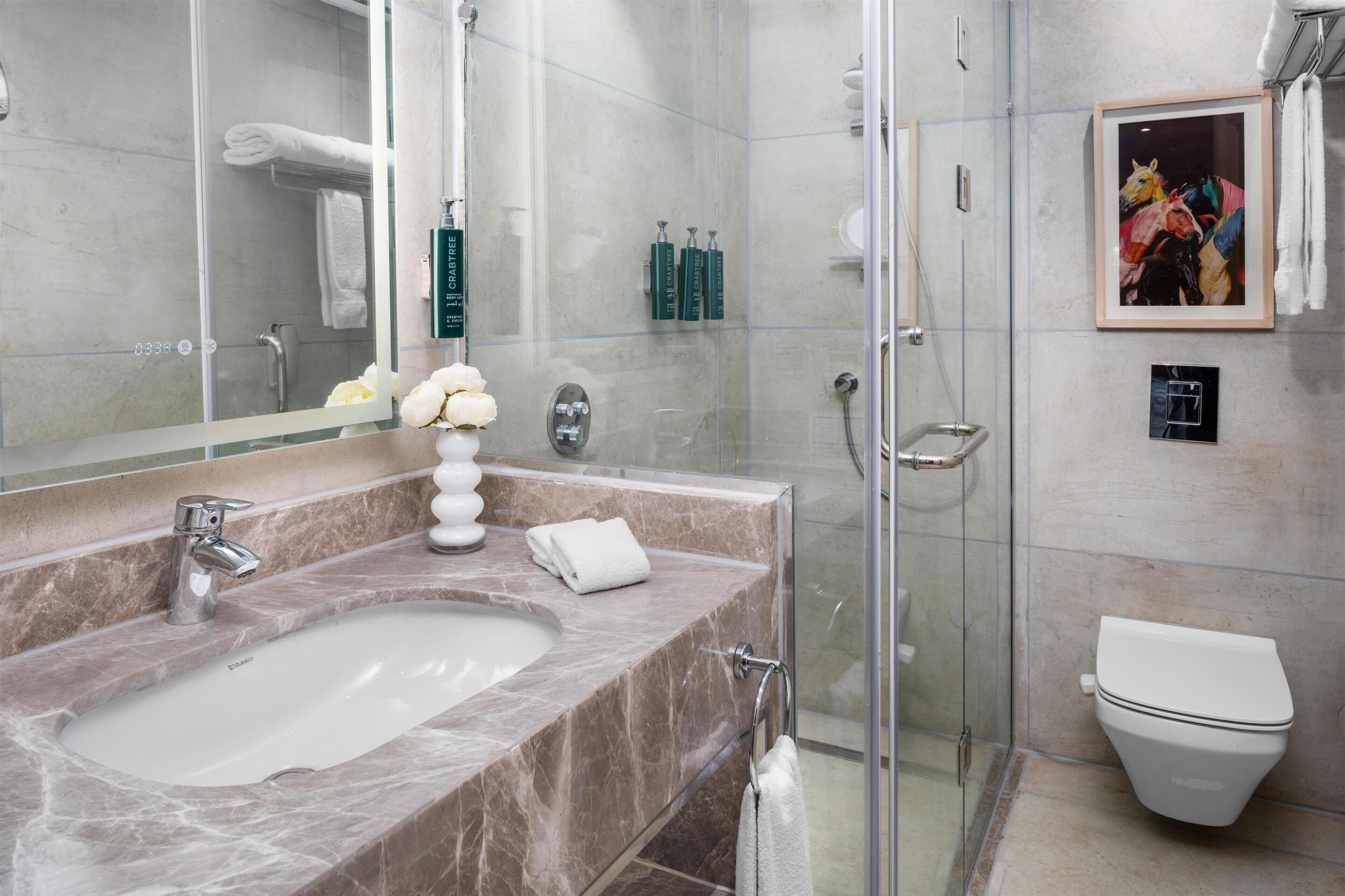 Ein modernes Badezimmer mit Marmorwaschbecken, einer Duschkabine aus Glas und einem gerahmten Bild an der Wand.