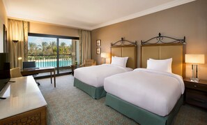A hotel room with two beds, a desk, a chair, a lamp, and a view of a pool. - Hilton Alexandria King's Ranch (Al-'Amriyah)