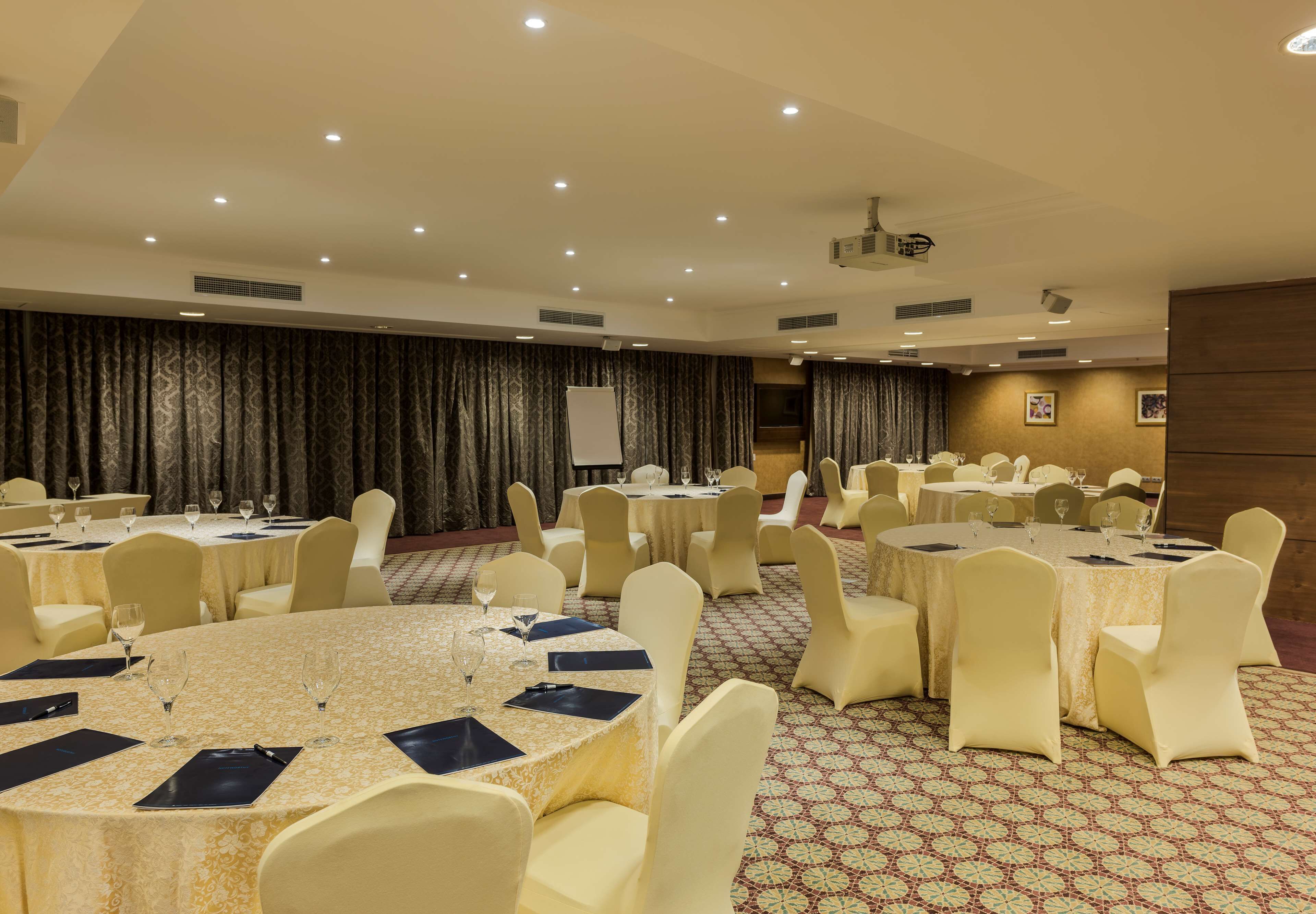 A conference room with round tables, white chairs, and a projector screen.