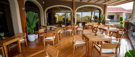A spacious outdoor dining area with wooden tables and chairs, potted plants, and a view of the surrounding landscape.