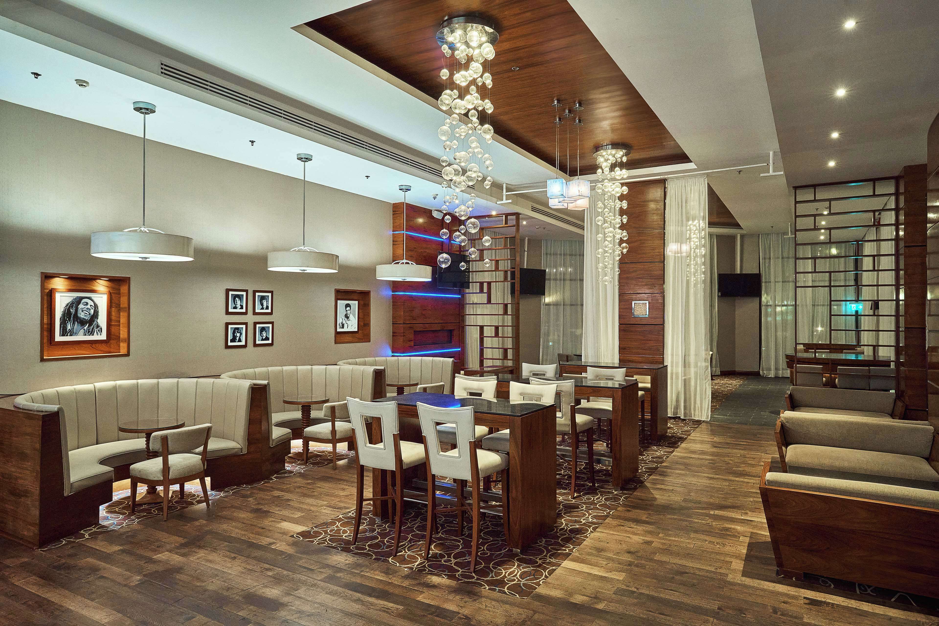 Un moderno vestíbulo de hotel con una zona de comedor central, disposición de asientos y una lámpara decorativa.