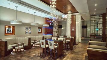 Un moderno vestíbulo de hotel con una zona de comedor central, disposición de asientos y una lámpara decorativa.