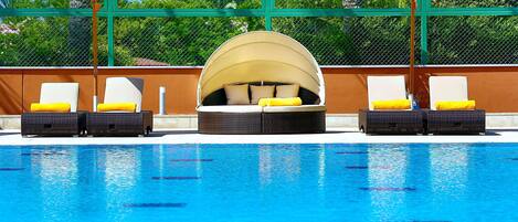 A pool area with lounge chairs and umbrellas, surrounded by a green fence and palm trees.