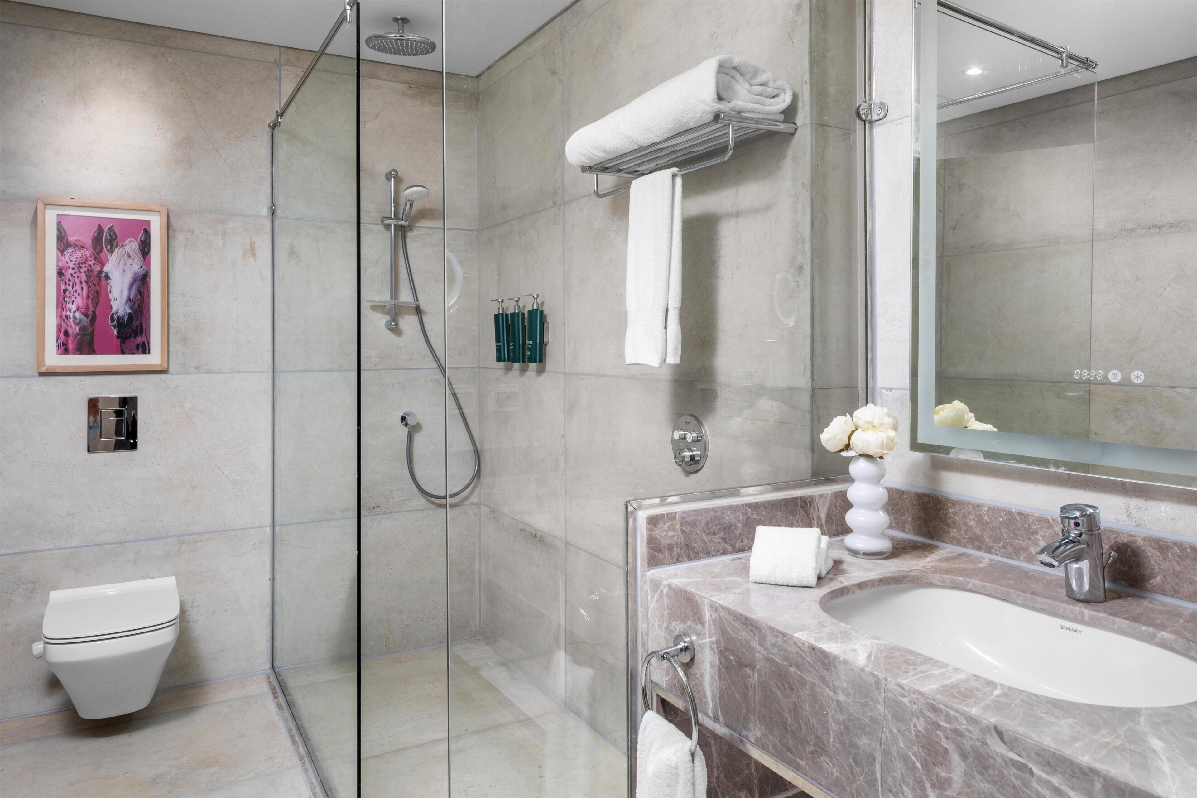A modern bathroom with a glass-enclosed shower, a marble sink, and a large mirror.