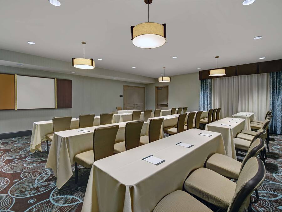 Une salle de conférence dotée de longues tables et de chaises, d’un écran de projection et d’un tapis à motifs.