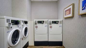 A laundry room with two front-loading washing machines and dryers, a tiled floor, and a framed picture on the wall.