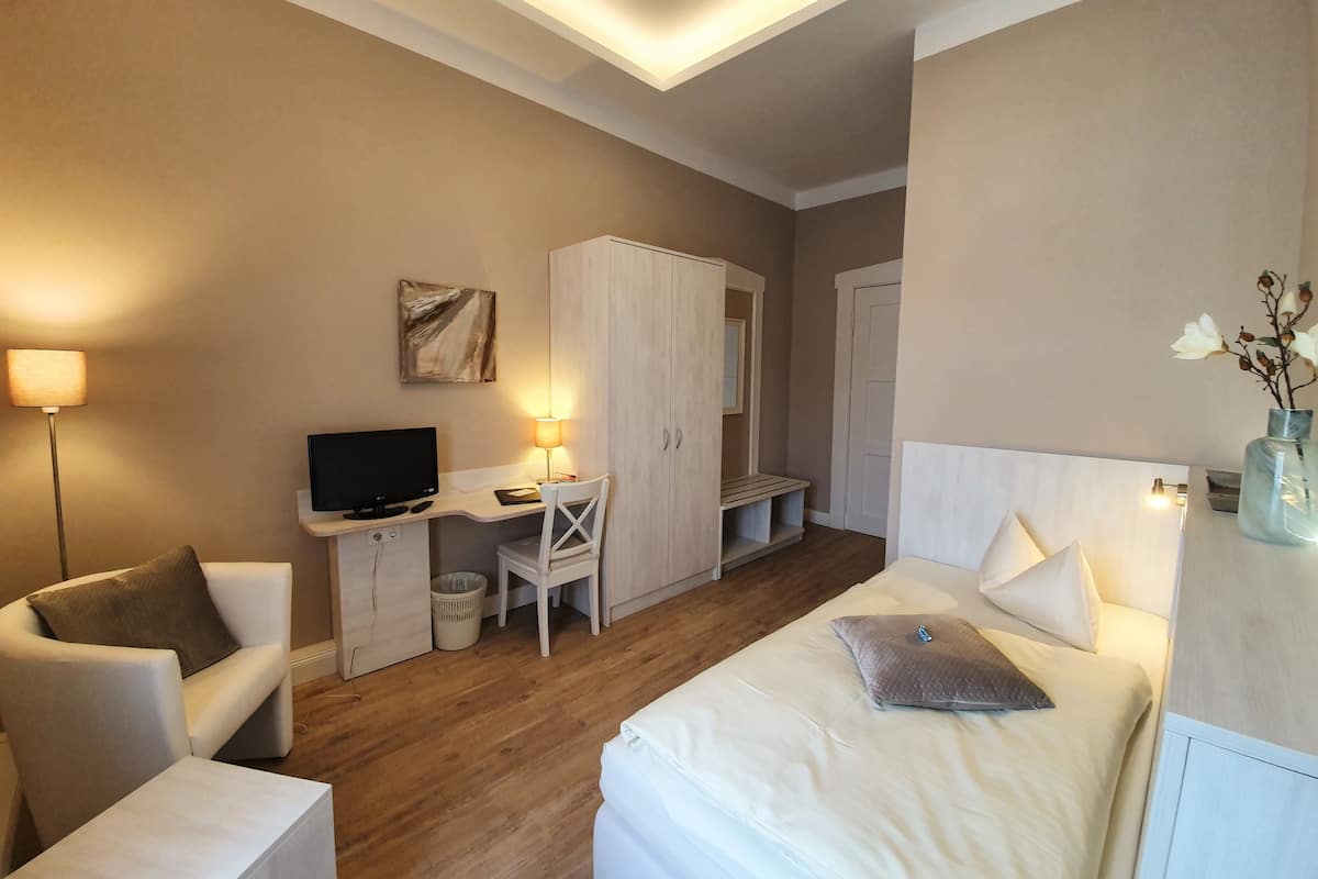 Ein Hotelzimmer mit Bett, Schreibtisch, Computer, Stuhl, Kleiderschrank und Lampe.