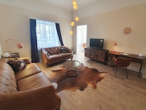 A modern living room with a leather sofa, a coffee table, a TV on a cabinet, and a desk with a chair. - Hotel Atlantic Travemünde (Lübeck)