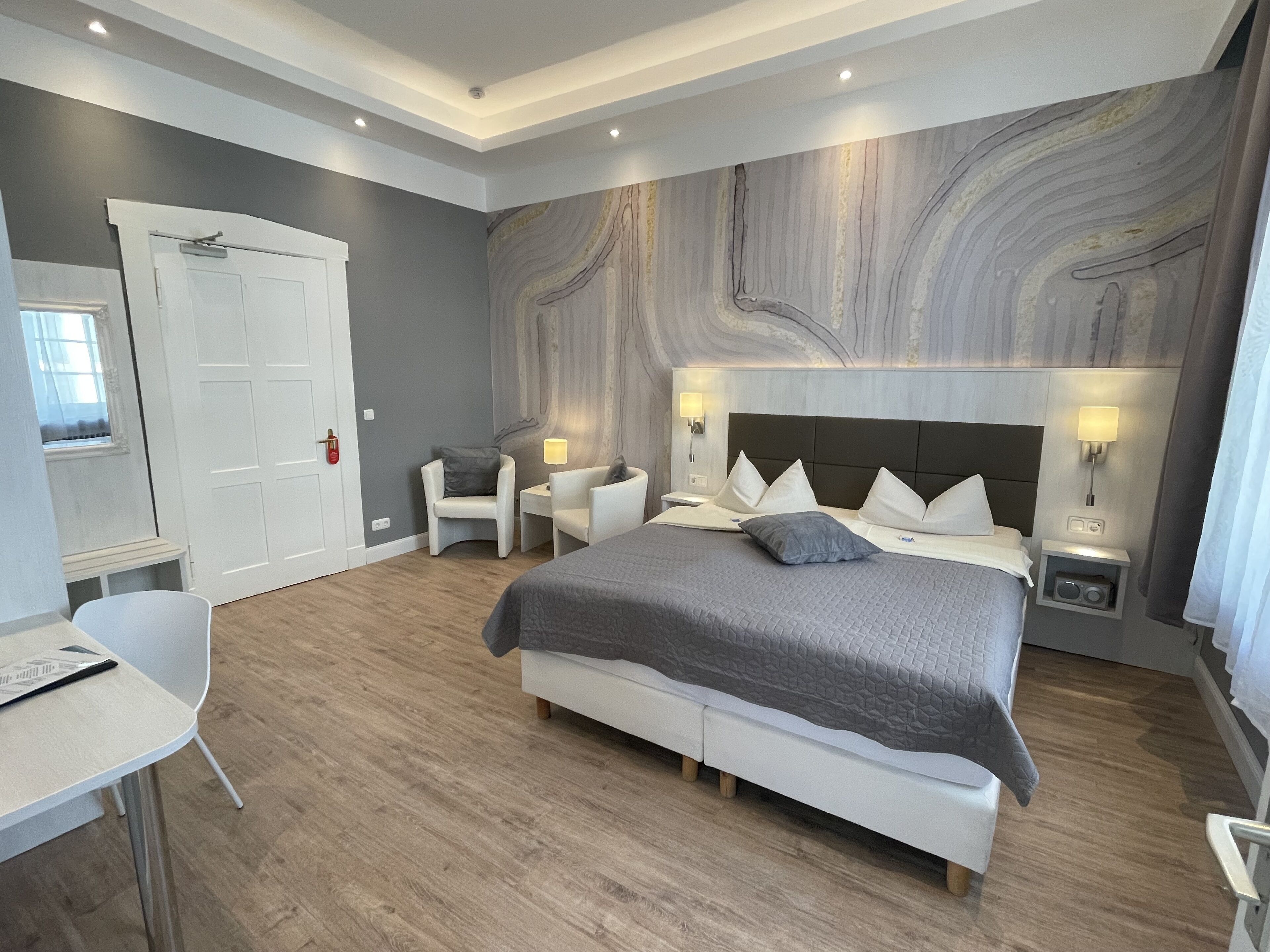 A modern bedroom with a large bed, bedside tables, a desk, and a chair.