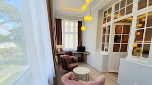 Ein Zimmer mit großem Fenster, Schreibtisch mit Computer, violetter Stuhl und ein kleiner runder Tisch.