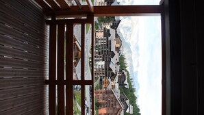 Une vue depuis un balcon en bois, avec en arrière-plan des montagnes, présentant un mélange de bâtiments modernes et traditionnels.