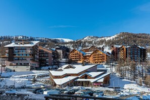 A ski resort with multiple wooden lodges, a parking area, and a backdrop of snow-covered mountains. - Noemys Déneb (Risoul)