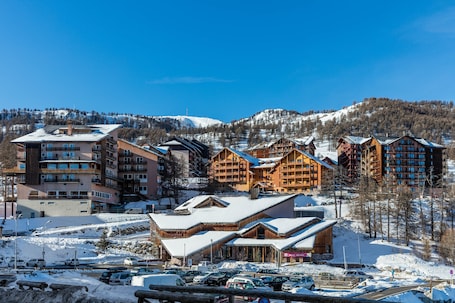 A ski resort with multiple wooden lodges, a parking area, and a backdrop of snow-covered mountains.
