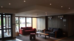 Un hall d’entrée spacieux, avec un canapé rouge, un canapé gris et une table basse en bois.