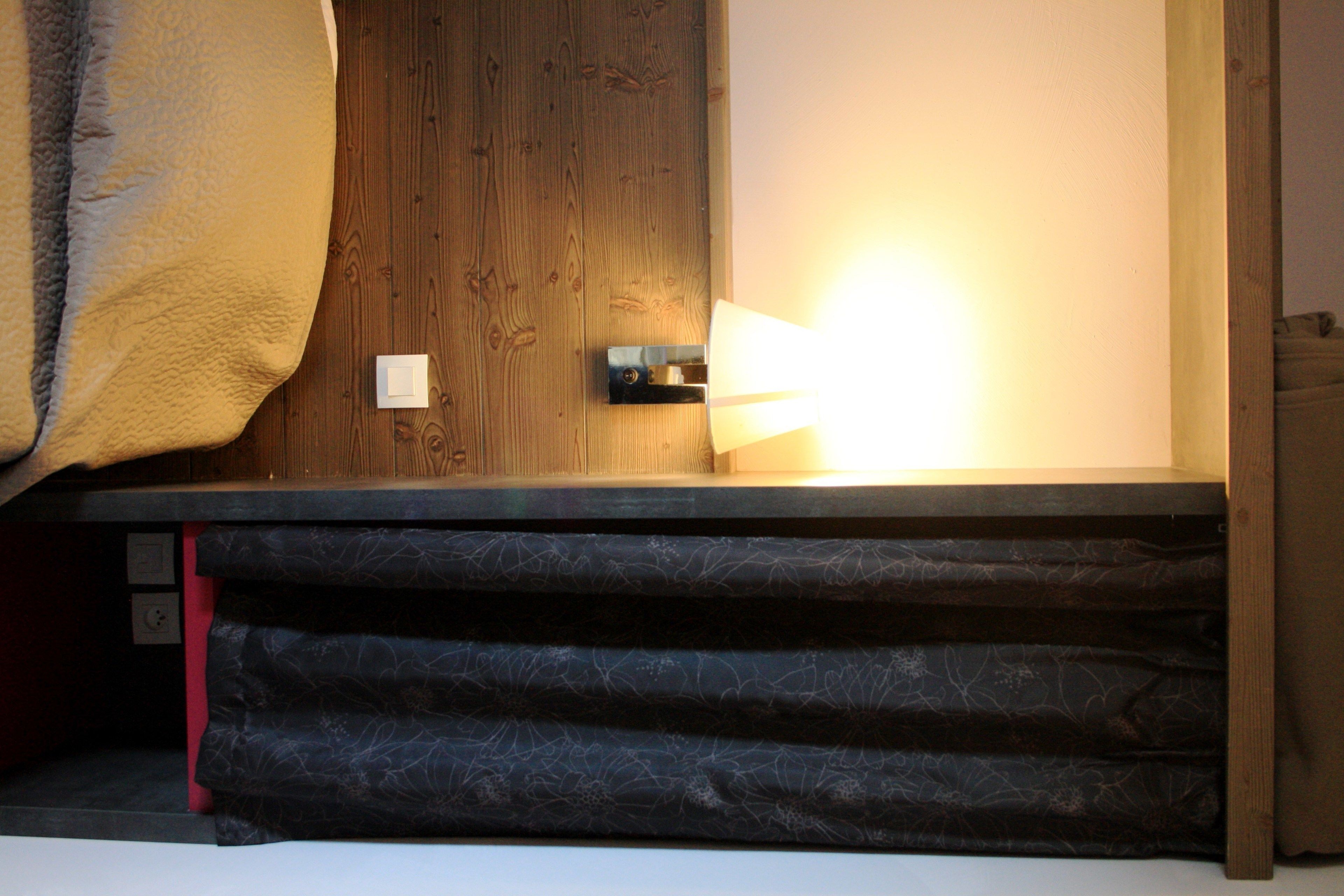 A room with a bed, a wooden door, and a wall-mounted light fixture.