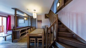 Un escalier en bois mène à une mezzanine aménagée avec une table à manger et des bancs.