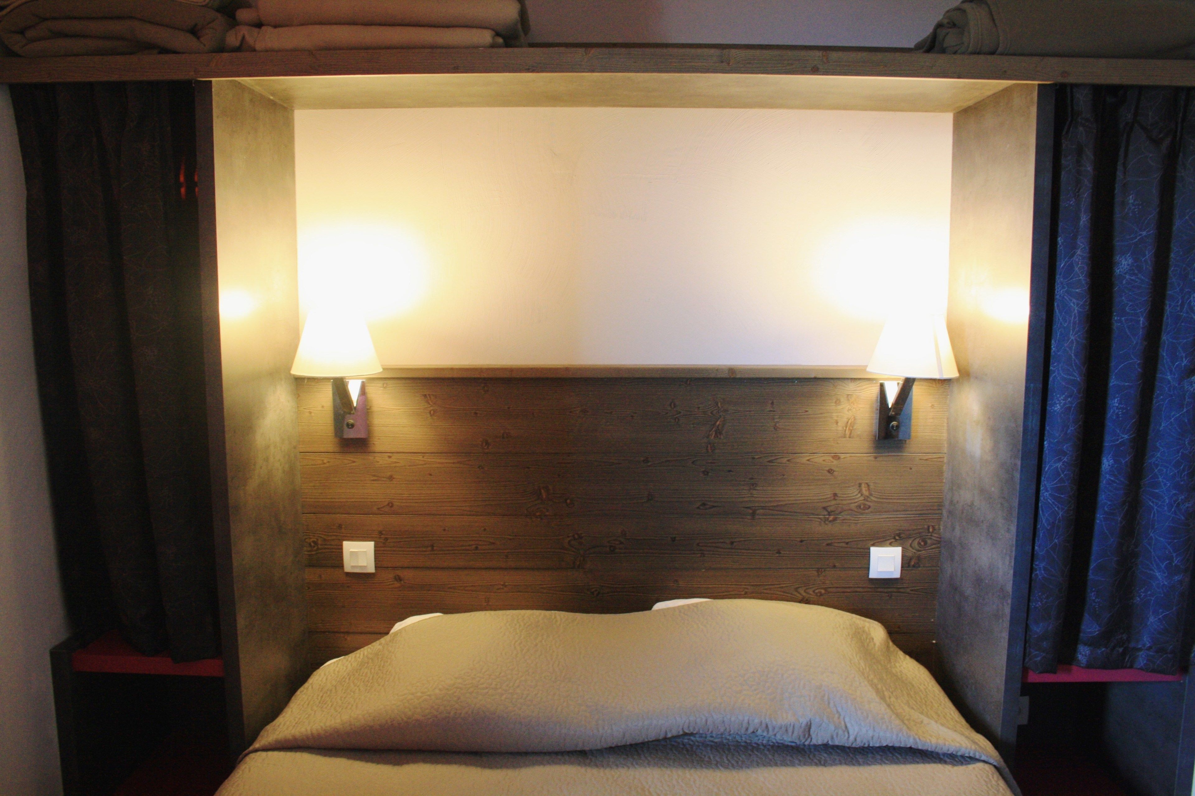 A bunk bed with two bedside lamps, wooden headboard, and curtains.
