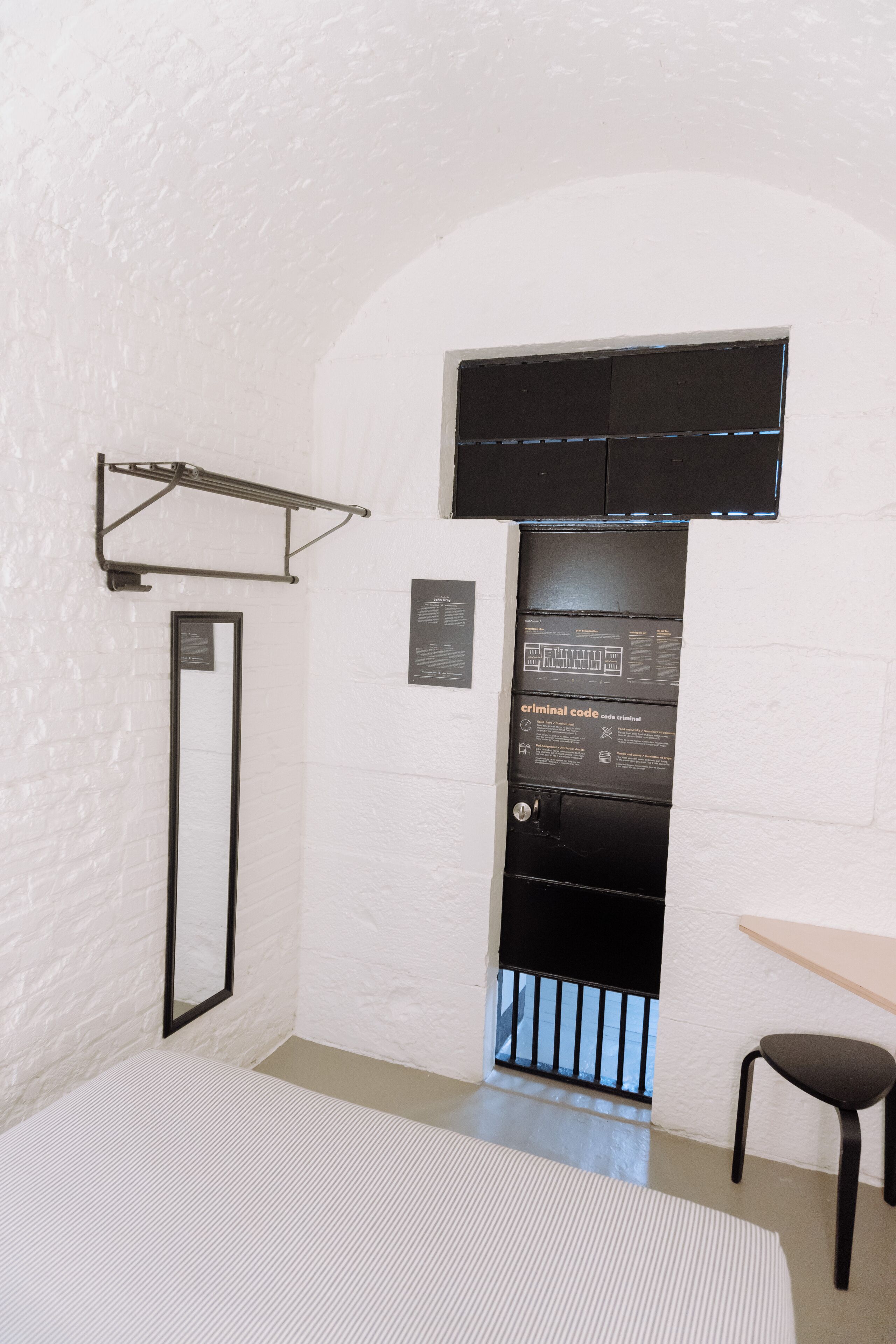 A room with a white brick wall, a black door with a window, a black metal rack, a black chair, and a striped rug.