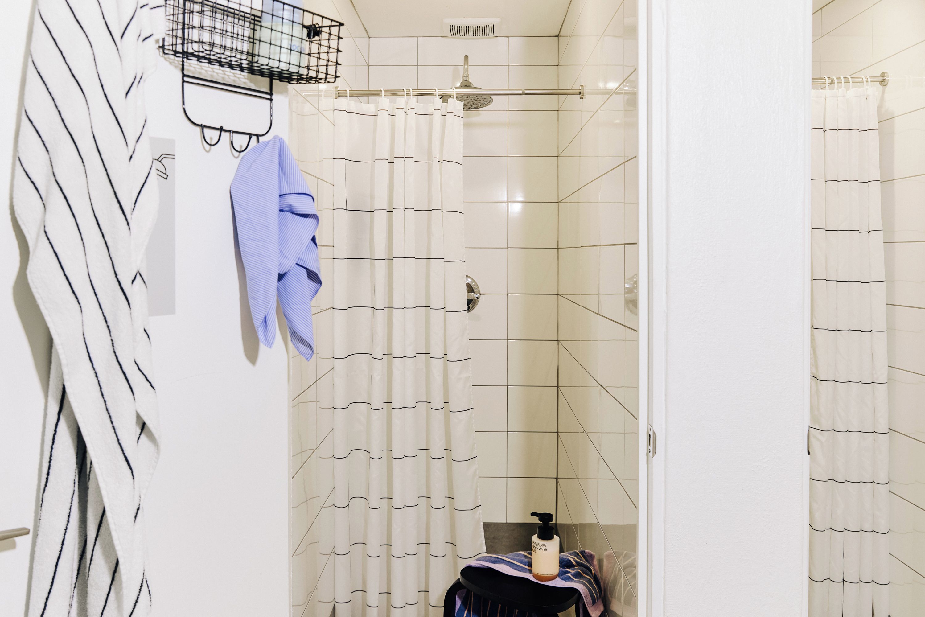 A bathroom with a shower, a towel rack, and a bottle of body wash on a towel.