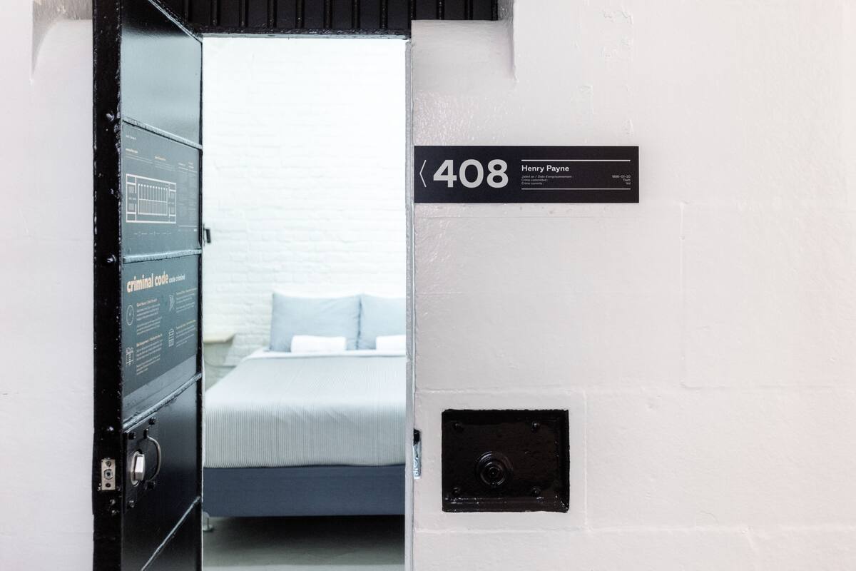 A hotel room with a bed, a wall-mounted sign indicating room number 408, and a small black panel on the wall.