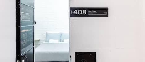 A hotel room with a bed, a wall-mounted sign indicating room number 408, and a small black panel on the wall.