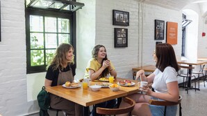 Three people dining at a wooden table with breakfast items. - Saintlo Ottawa Jail Hostel (Ottawa)