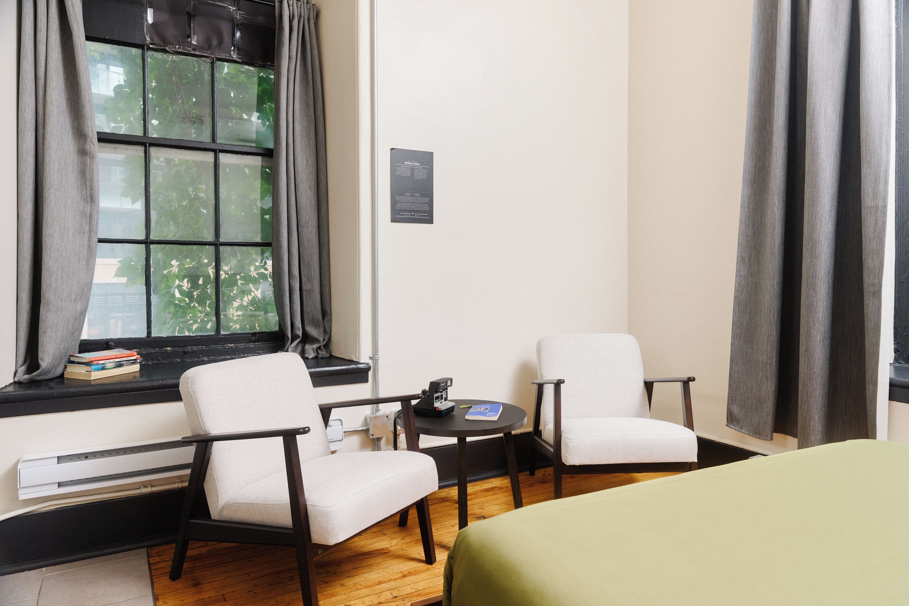 A hotel room with a bed, two chairs, a small table, and a window with curtains.