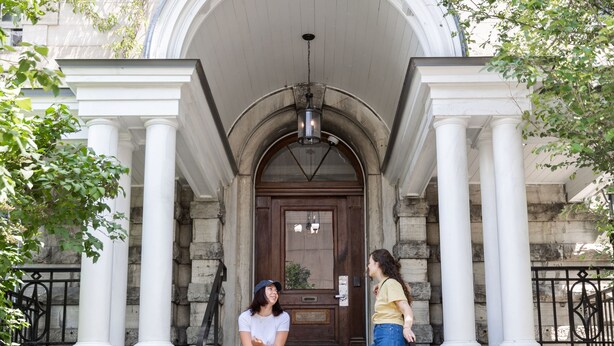 A building entrance with a stone facade, white columns, and a wooden door. - Saintlo Ottawa Jail Hostel (Ottawa)