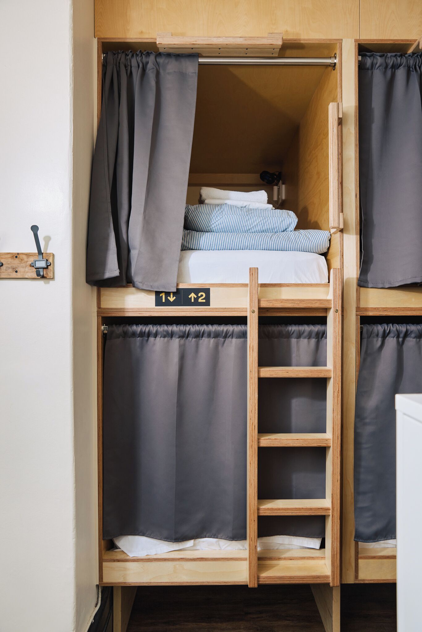 Un lit superposé avec une échelle, une petite étagère avec des vêtements pliés et un panneau indiquant la direction des toilettes.