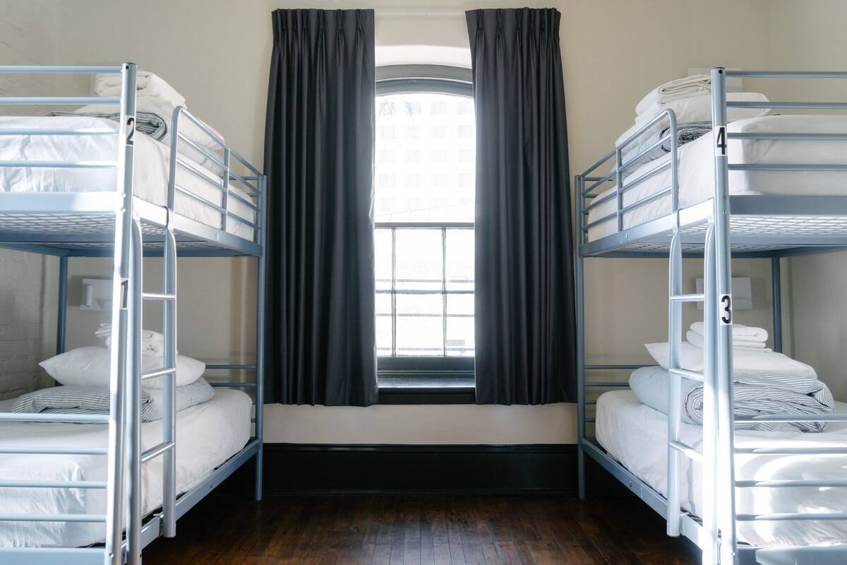 A room with two bunk beds, a window with curtains, and wooden flooring.