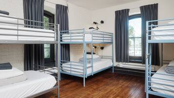A dormitory room with bunk beds, a window with curtains, and a wall-mounted fan.