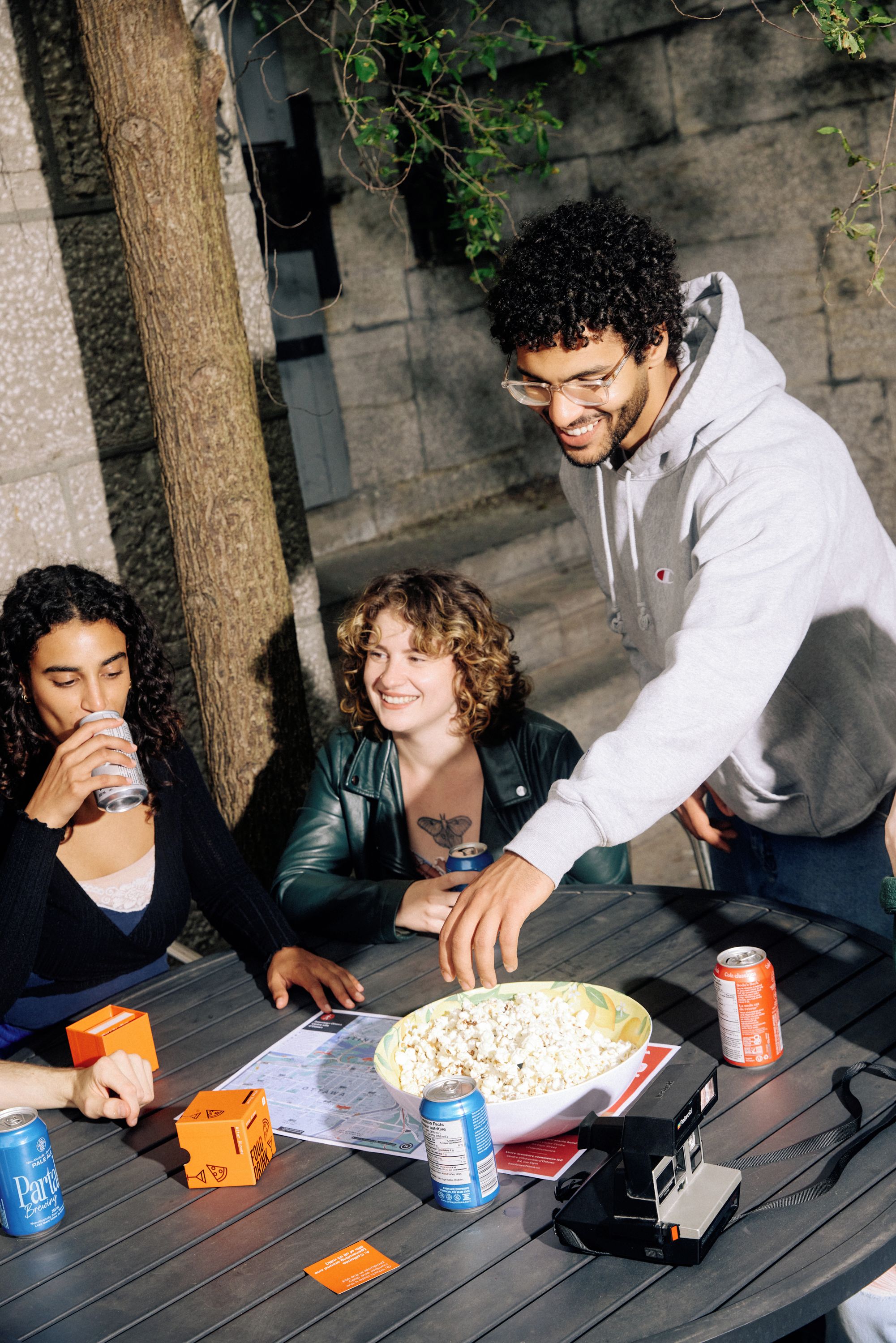 A group of people at an outdoor table with a bowl of popcorn, drinks, and a map.