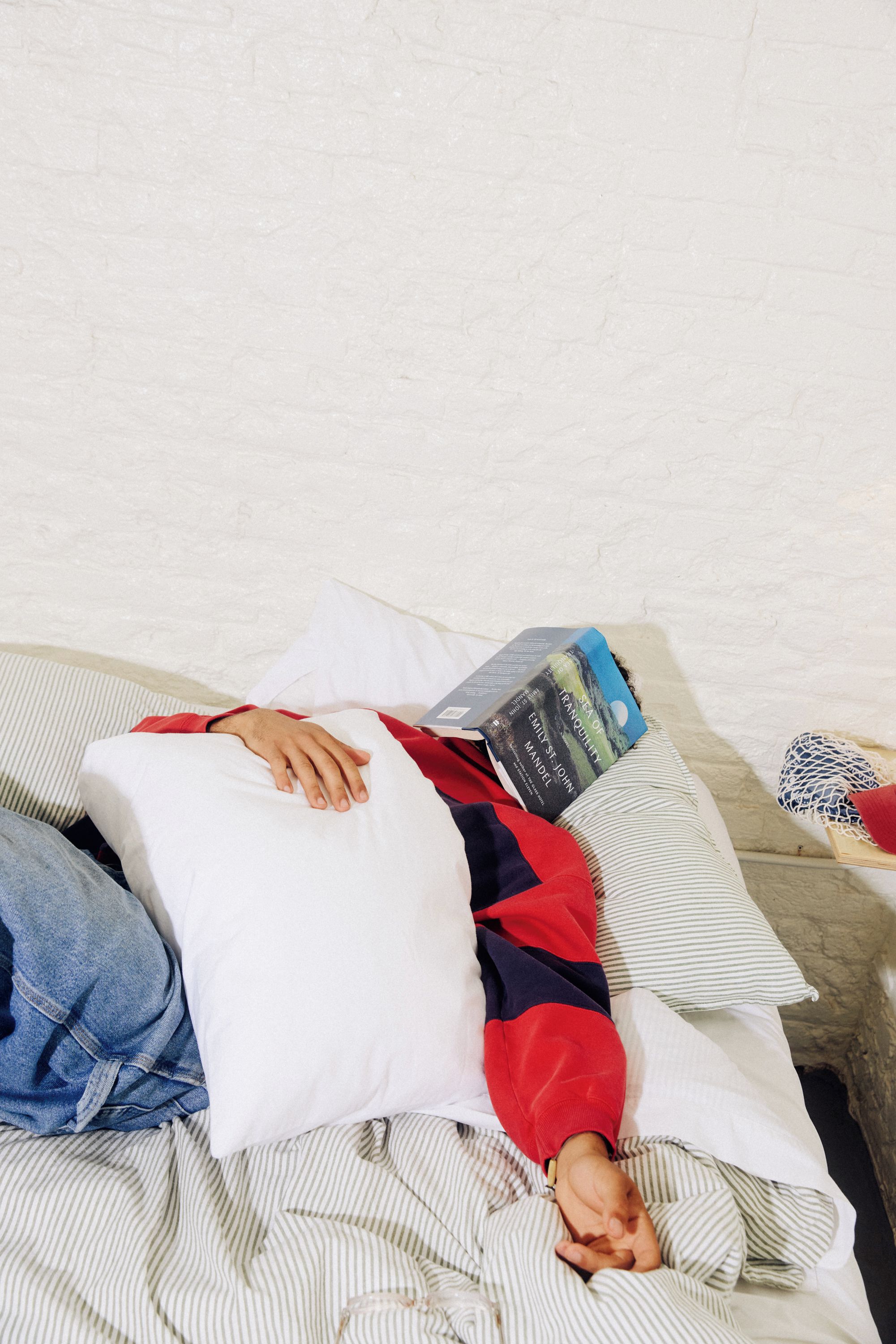 A person lying on a bed with a book and a pillow.