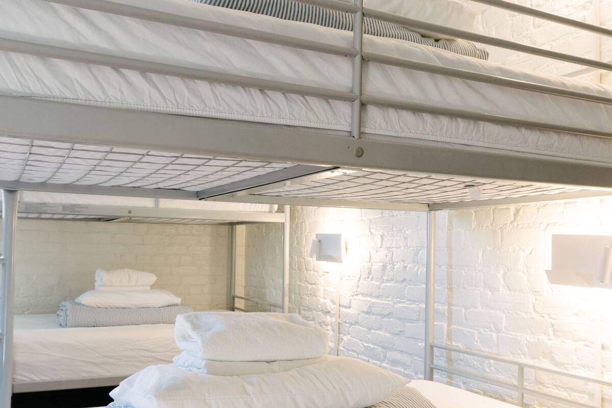 A bunk bed room with white bedding and a brick wall.