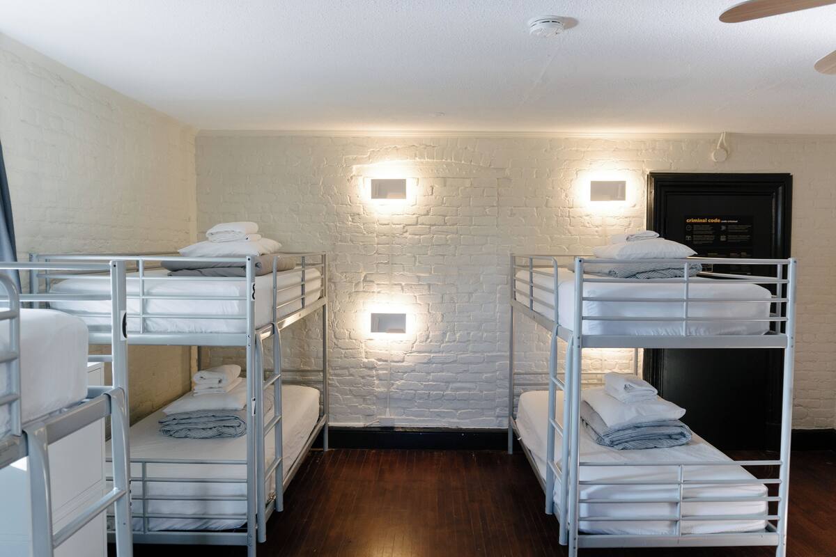 A bunk room with white metal bunk beds, a brick wall, and two wall-mounted lights.