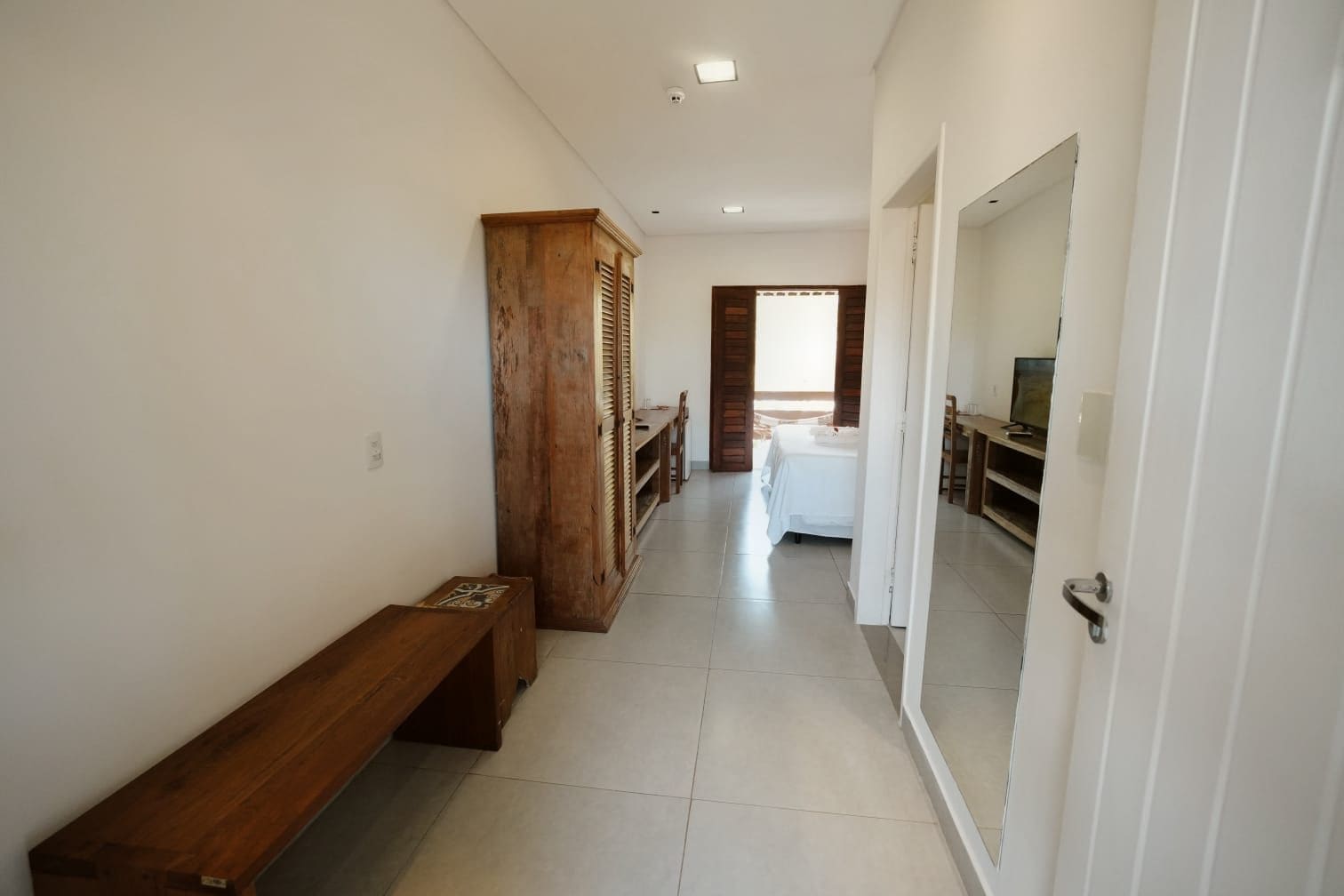 Un pasillo con un banco de madera, una cama y un televisor en la habitación.